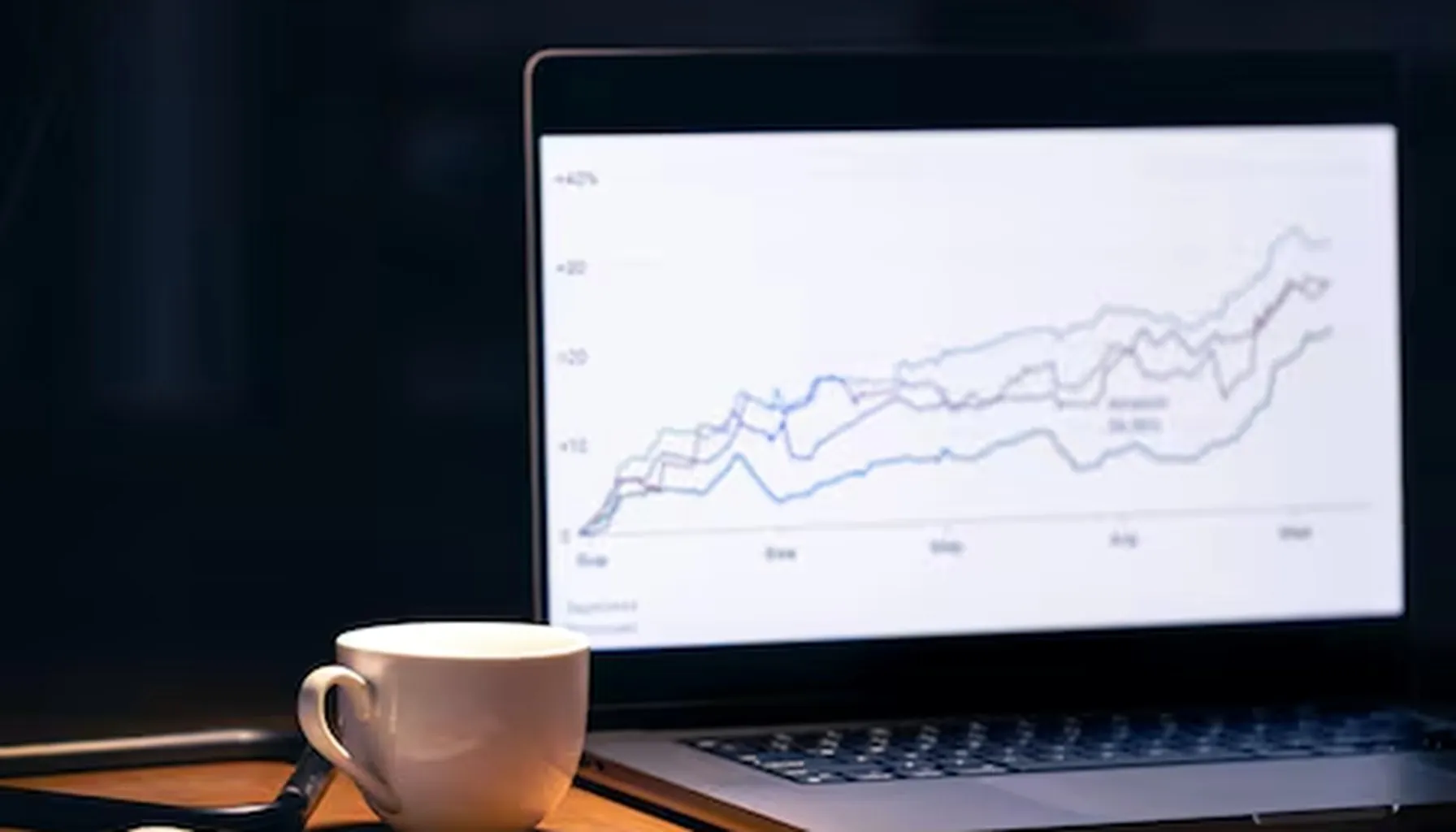 A consultant's desk with a laptop showing rising analytics, coffee and a notebook